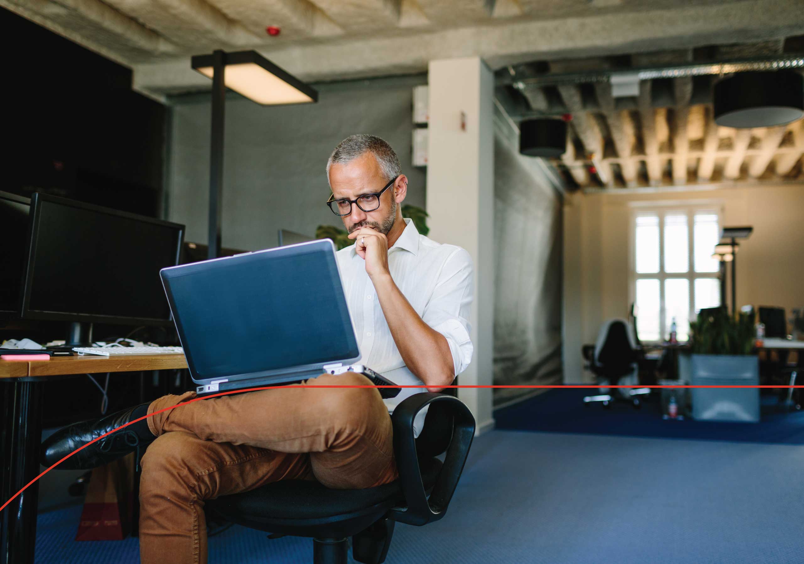 Male business owner sitting at desk with their laptop on their lap, reviewing commercial insurance coverage for their business.